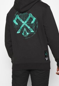 Felpa nera con un grafico turchese di asce incrociate e un design circolare sul retro, con un'etichetta del logo Reebok in basso.
