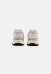 Béžové a šedé tenisky New Balance s vrstevnatým designem, vyrobené z semiše a síťoviny, s bílou mezipodešví a černou podešví.