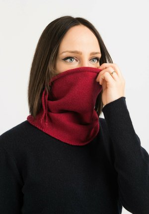 Tour de cou en tricot rouge fabriqué en tissu doux, présentant une coupe ajustée avec des liens réglables et une texture lisse, porté par-dessus un pull sombre.