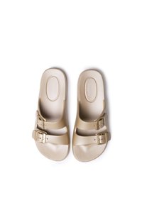 Beige slip-on sandals made of textured plastic, featuring two adjustable straps with metallic buckles. Smooth footbed with slight arch.
