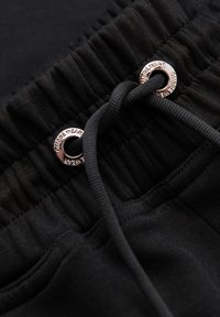 Ceinture élastique noire avec cordon passant à travers des œillets métalliques gravés "OMBRE WEAR" sur tissu noir.