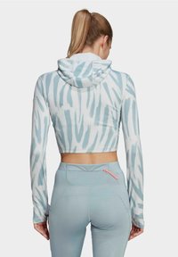 Femme avec une queue de cheval blonde portant un hoodie court blanc et bleu clair à motifs et un legging taille haute bleu clair avec une petite poche zippée.