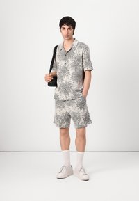 Kortermet skjorte med knapper og shorts i et grått og hvitt abstrakt mønster, kombinert med hvite sneakers og en svart crossover-veske.