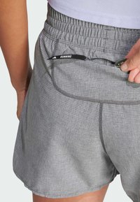Pantalones cortos de running grises hechos de material ligero, con un patrón de cuadrícula texturizado, cinturilla elástica y un pequeño bolsillo con cremallera y tirador.