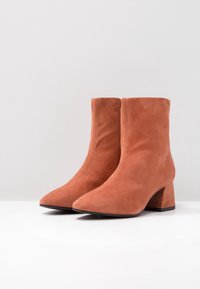 Suède enkellaarsjes in een gedempt oranje met een spitse neus en een blokhak. Glad textuur met een strakke, minimalistische stijl.