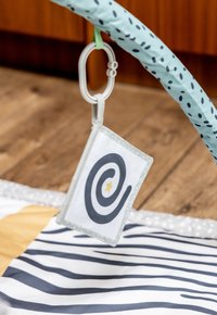Activity mat with a blue, padded arch. Features a white card with spiral design and star, attached via a gray clip. Striped patterns on mat.