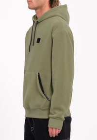 Olijfgroen hoodie met een kangoeroezak en zijrits, gekenmerkt door een zwart logo-embleem en zwarte trekkoorden met witte accenten.