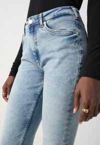 Jeans in denim azzurro chiaro con una vestibilità slim, caratterizzati da un classico design a cinque tasche, chiusura con bottone metallico e dettagli di sbiadimento sottili.