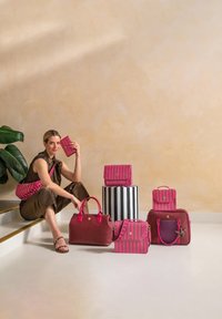 Collectie van tassen in roze en bordeauxrood, met gestreepte patronen en verschillende vormen, op een witte vloer met een beige muur op de achtergrond.