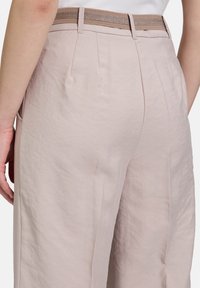 Světlé růžové široké kalhoty z texturované tkaniny. Jsou vybaveny hnědým elastickým pasem a bočními kapsami pro větší praktičnost.