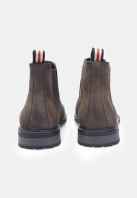 Botas Chelsea de ante marrón con paneles laterales elásticos, suela de goma y tiradores a rayas. Presentan una textura suave y una silueta redondeada.