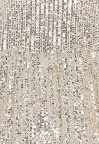 Tessuto con paillettes nei toni dorati, caratterizzato da una combinazione di paillettes circolari lucide disposte in linee verticali su uno sfondo morbido e testurizzato.