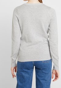 Helles graues Sweatshirt mit langen Ärmeln, rundem Halsausschnitt, gerippten Bündchen und Saum; über blauen Jeans getragen und zeigt eine weiche Textur.