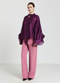 Lila Satinbluse mit lockeren Ärmeln und Halber, kombiniert mit rosa weit geschnittenen Hosen, die einen Akzent am Saum haben. Glatte Texturen in der gesamten Kleidung.