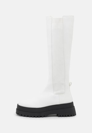 Tall white leather boot with ribbed elastic side panel and chunky black lug sole, shown from the outer side on a white background.