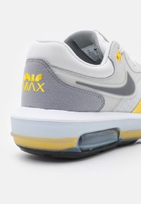 Nike Air Max-sneaker med en grå ovandel och gula accenter, en transparent luftdämpningsenhet och textil runt kragen.