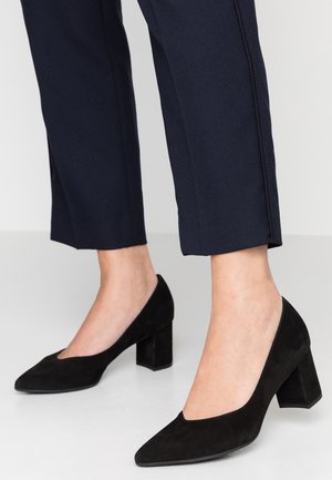 Des escarpins en suède noir à bout pointu et à talon bloc, associés à un pantalon cropped bleu marine avec une finition texturée et des fentes latérales.