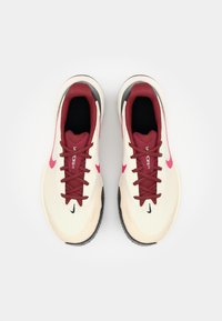 Beige løpesko med maroon-detaljer og lisser, teksturert overdel, svart yttersåle, og et Nike-logo på siden, som viser et strømlinjeformet design.