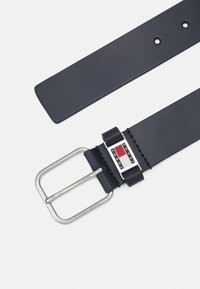 Cintura in pelle blu navy con una fibbia in metallo argentato. La fibbia presenta un logo rettangolare in rosso, bianco e nero, con dettagli cuciti.