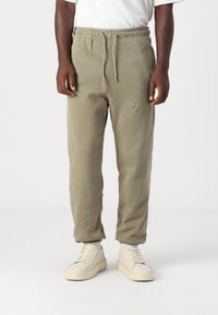 Grågrønne joggebukser med elastisk midje og snor, med innsnevrende ben og ribbestrikkede mansjetter, sammen med lyse sneakers.