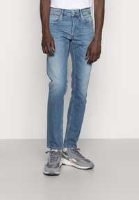 Jeans de mezclilla azul claro con un corte recto, que presentan un desvanecimiento sutil, cinco bolsillos y un cierre de botón. Se llevan con zapatillas deportivas grises.