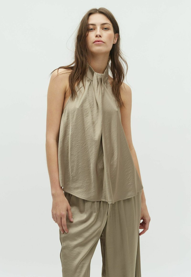 Sleeveless halterneck top in light khaki fabric, featuring a flowing design with soft drapes and a smooth, slightly glossy texture.