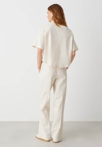 Top corto cremoso con maniche corte, abbinato a pantaloni larghi cremosi. Tessuto morbido, vestibilità rilassata, design minimalista senza decorazioni.