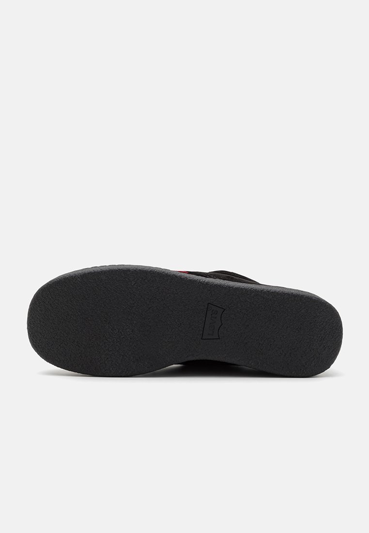 Semelle de chaussure en caoutchouc noir avec surface texturée, arborant un logo de marque. Sa forme est plate avec un large talon pour plus de stabilité.