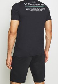 Svart bomullströja med rund halsringning, korta ärmar och ett tryckt logotyp och text på baksidan; matchas med svarta shorts.