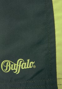 Zelená tkanina s hladkou textúrou, ktorá obsahuje žltý akcentový pruh a logo "Buffalo" v kurzívnom žltom písmene v ľavom dolnom rohu.