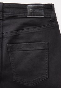 Pantalones de mezclilla negros con un acabado texturizado, que cuentan con un bolsillo cuadrado y un parche de cuero con la marca en la cinturilla.