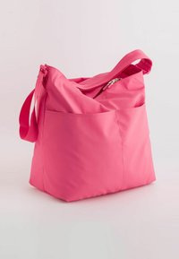 Pink nylon bag with a slouchy design, zip closure, and a front pocket. Features a fabric strap for carrying and a smooth texture.