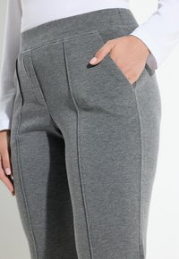 Pantalones de chándal grises hechos de una tela suave, con dos bolsillos laterales, frente plano y un acabado liso con costuras visibles.