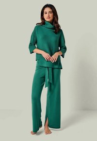 Grünes gestricktes Set mit einem gerippten Rollkragenpullover und weit geschnittenen Hosen mit einem Bindegürtel. Beide Teile haben eine weiche Textur und eine entspannte Passform.