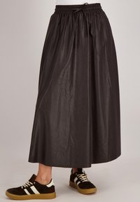 Zwarte, lange rok van lichtgewicht materiaal met een elastische tailleband en trekkoorddetail, gecombineerd met donkere sneakers met witte strepen.