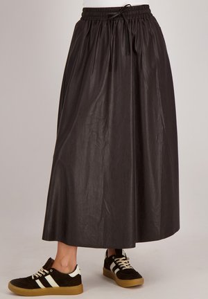 Zwarte, lange rok van lichtgewicht materiaal met een elastische tailleband en trekkoorddetail, gecombineerd met donkere sneakers met witte strepen.