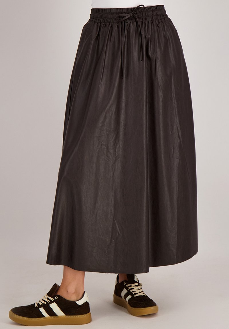 Zwarte, lange rok van lichtgewicht materiaal met een elastische tailleband en trekkoorddetail, gecombineerd met donkere sneakers met witte strepen.
