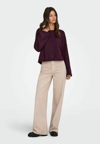 Suéter de corte holgado y manga larga en púrpura profundo, combinado con pantalones de pierna ancha en beige claro y zapatos de suela gruesa negros.