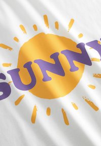 Weißes Baumwoll-T-Shirt mit einem großen gelben Sonnenmotiv, dessen Strahlen nach außen ausstrahlen, und fettgedrucktem lila Text, der "SUNNY" lautet.