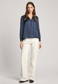 Ναυτικό μπλουζάκι από ελαφρύ, γυαλιστερό ύφασμα, με σχέδιο από κουκίδες, κούμπωμα μπροστά και μακριά μανίκια; συνδυασμένο με κρεμ παντελόνι σε φλαρέ γραμμή.