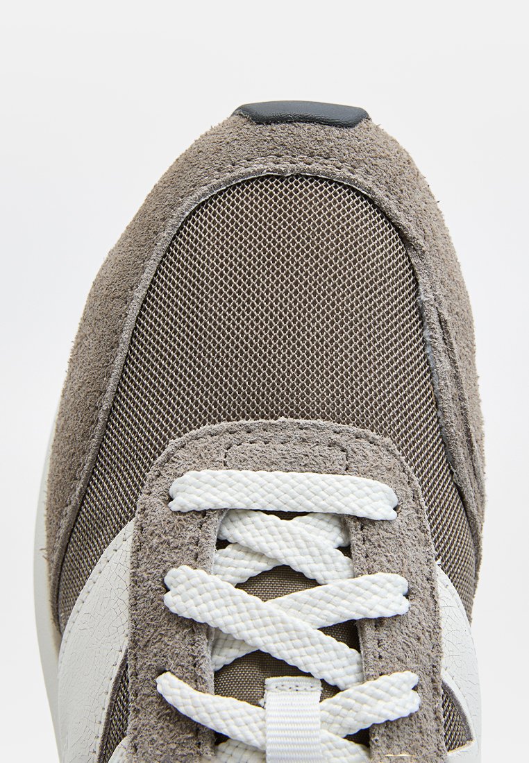 Grauer Sneaker aus Wildleder und Mesh mit weißen Schnürsenkeln, strukturiertem Obermaterial, abgerundeter Zehenpartie und kontrastierendem weißen Seitenpaneel. Robuste Gummisohle.