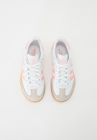 Witte sportschoenen met roze strepen, een grijze suède neuskap en witte veters. Glad materiaal met een rubberen zool met textuur.