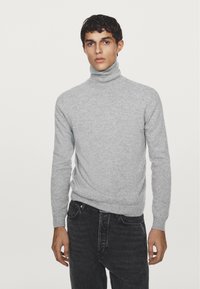 Pullunder grigio chiaro in maglia fine e morbida. Design aderente con maniche lunghe e polsini a costine. Abbinato a jeans scuri.