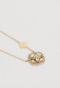 Gold necklace with a floral pendant, embellished with clear crystals. Chain features a logo charm. Smooth surface, elegant design.