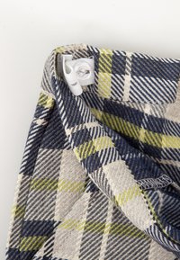 Tela de cuadros con colores azul, gris y verde lima, con un patrón de espiga. Incluye una banda elástica blanca y un ajuste con toggle.