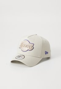 Beige baseball cap med et struktureret Los Angeles Lakers-logo i lilla og guld. Inkluderer en buet skygge og justerbar snapback-design.