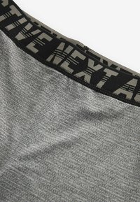 Grå atletiske shorts med et tekstureret stof, der har en sort taljeledning mærket "NEXT." Korte syninger er synlige.