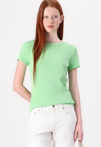Lys grøn ribbet t-shirt med korte ærmer og rund halsudskæring, parret med hvide bukser, der viser en tætsiddende pasform og blød tekstur.