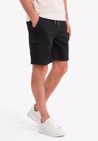 Shorts cargo noirs au coupe décontractée, fabriqués en tissu coton durable, avec des poches latérales et une taille à cordon. Associés à des baskets blanches.