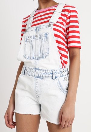 Persona vistiendo un peto corto de mezclilla blanca desgastada y una camiseta de manga corta con rayas horizontales rojas y blancas.